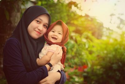 Portrait of young woman carrying happy daughter against trees