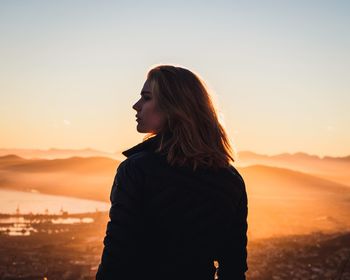 Woman standing on landscape against clear sky during sunset