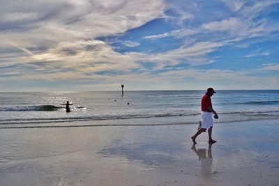 Side view of man walking on wet shore at beach against sky