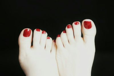 Low section of woman with red nail polish against black background