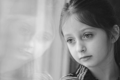 Close-up of thoughtful cute girl looking through window