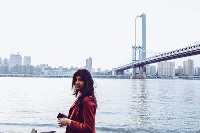 Portrait of young woman standing by east river in city