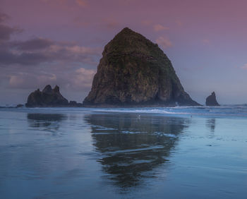 Rock formation in sea against sky during sunset