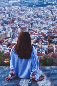 Rear view of woman sitting against buildings in city