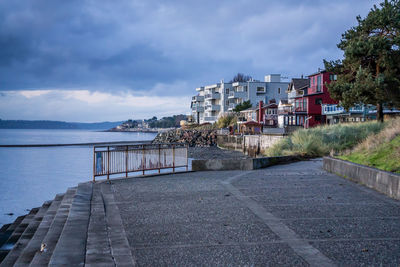 Footpath by sea against sky in city