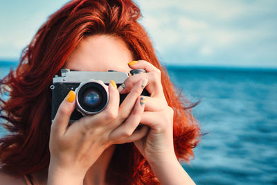 Red haired woman travel photographer, taking pictures on the background of the sea. 