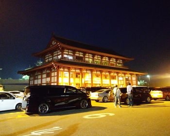 Cars on road by illuminated building against sky at night