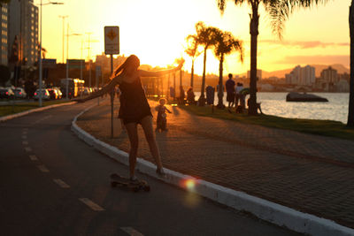 Young woman skateboarding on street during sunset