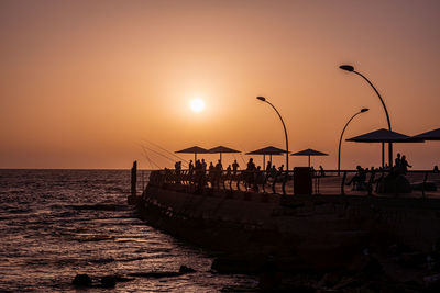 Silhouette people on beach against sky during sunset