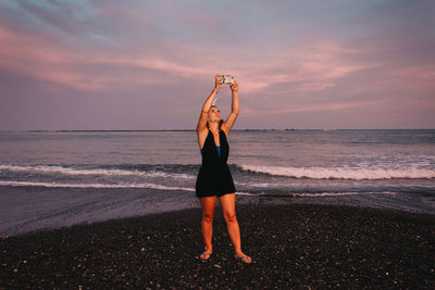 Rear view of woman standing at beach against sky during sunset