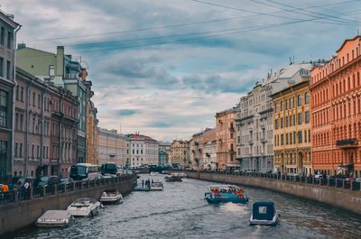 Boats in canal amidst buildings in city against sky