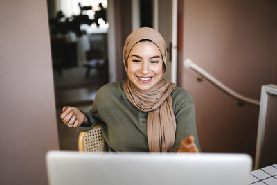 Smiling female freelancer in hijab doing video call through laptop at home
