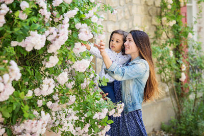 Mother and little handsome baby boy looking at bush with white roses