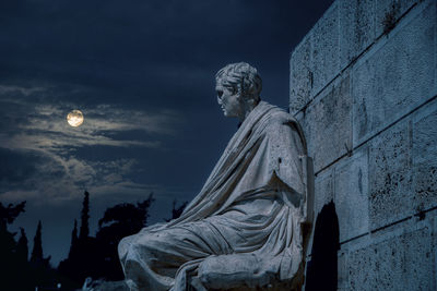 Low angle view of ancient statue of poet against sky during full moon in athens.