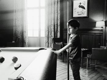 Boy holding cue by pool table at home