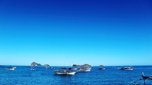 Boats on sea against clear blue sky