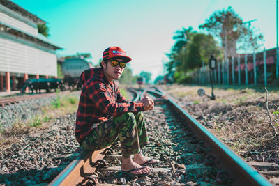 Man with arms outstretched on railroad tracks against sky