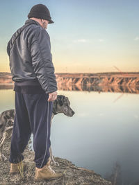 Man with dog standing by lake against sky