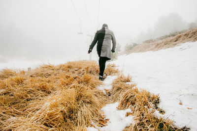 Rear view of man walking on snowy field