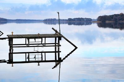 Scenic view of wooden pier mirrored in lake against sky