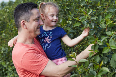 Smiling father with daughter touching plants at agricultural field