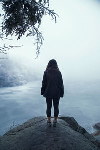 Rear view of woman standing on rock against sky