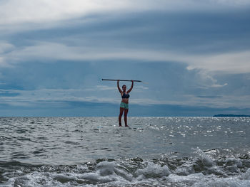 Full length of young woman standing on paddle board in the sea against sky