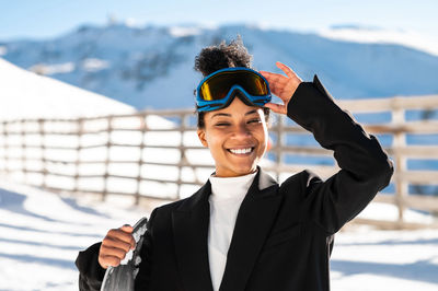 African american woman with goggles and a snowboard on a snowy mountain during winter