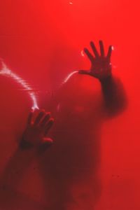 Close-up of hand touching glass against red background