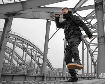 Low angle portrait of ninja man practicing martial arts on bridge against sky