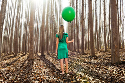 Rear view of woman holding balloon while standing in forest