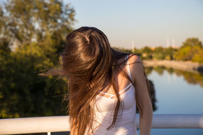 Young woman with tousled hair standing by railing over river