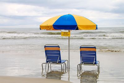Deck chairs on beach against sky
