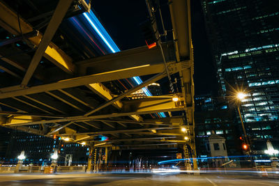 Illuminated light trails on road amidst buildings in city at night