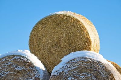 Low angle view of hay bales on field against clear blue sky