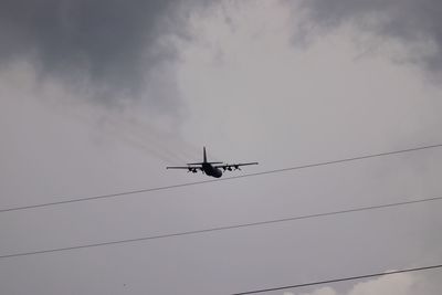 Low angle view of silhouette airplane against cloudy sky