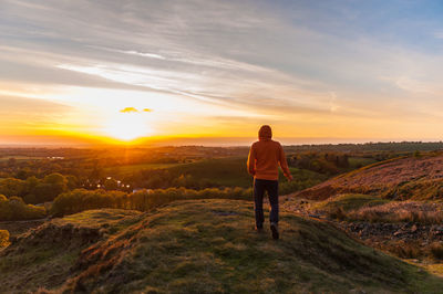 Rear view of man standing on landscape against sunset sky