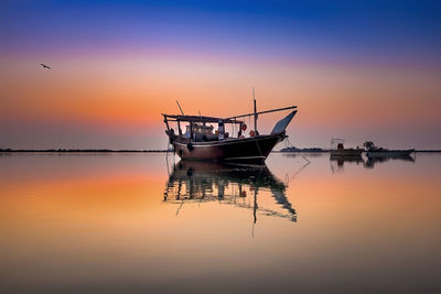 Fishing boat moored in sea against sky during sunset