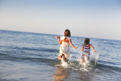 Rear view of sisters running on seashore against sky