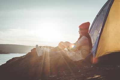 Woman sitting by tent on mountain against sky