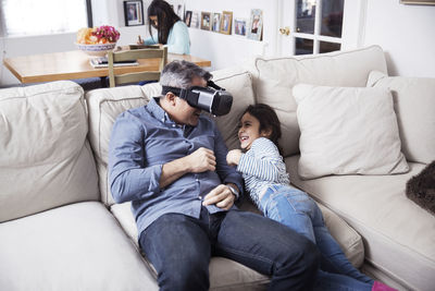 Playful father wearing virtual reality simulator while playing with daughter at home