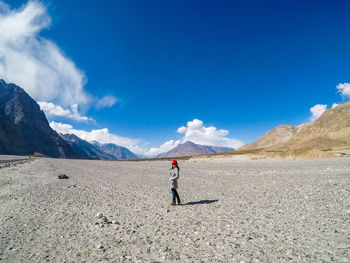 Full length side view of woman standing on arid landscape against sky during sunny day