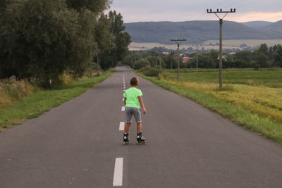 Rear view of boy roller skating on road 