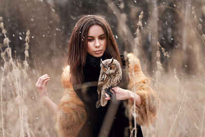 Young woman with owl standing on field