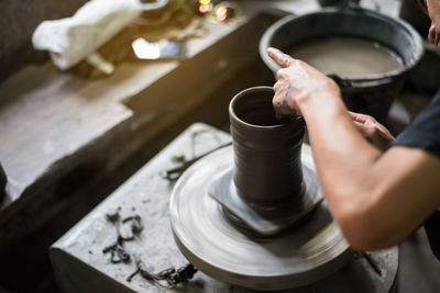 Midsection of porter making container on pottery wheel at workshop