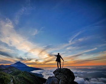 Silhouette man standing on rock against sky during sunset