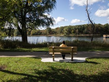 Rear view of woman sitting on bench against lake