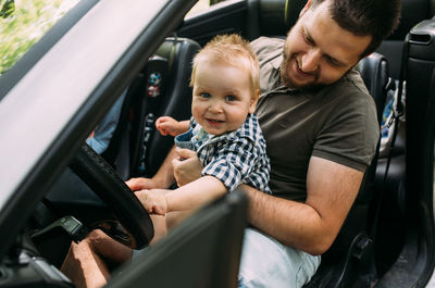 Dad shows his little son how to drive car while sitting behind wheel