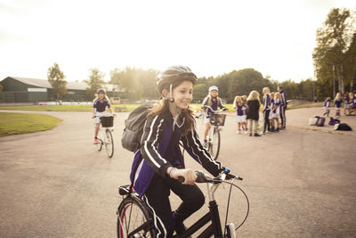 Girl cycling on footpath with friends against sky