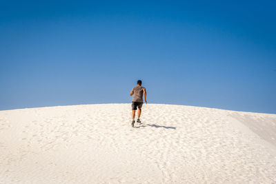 Rear view of man standing on desert against clear blue sky